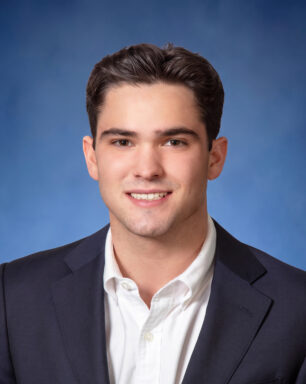Smiling young man in a navy blazer and white shirt against a blue studio backdrop